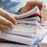 Businesswoman,Working,In,Stacks,Of,Paperwork,Files,For,Searching,Infomation